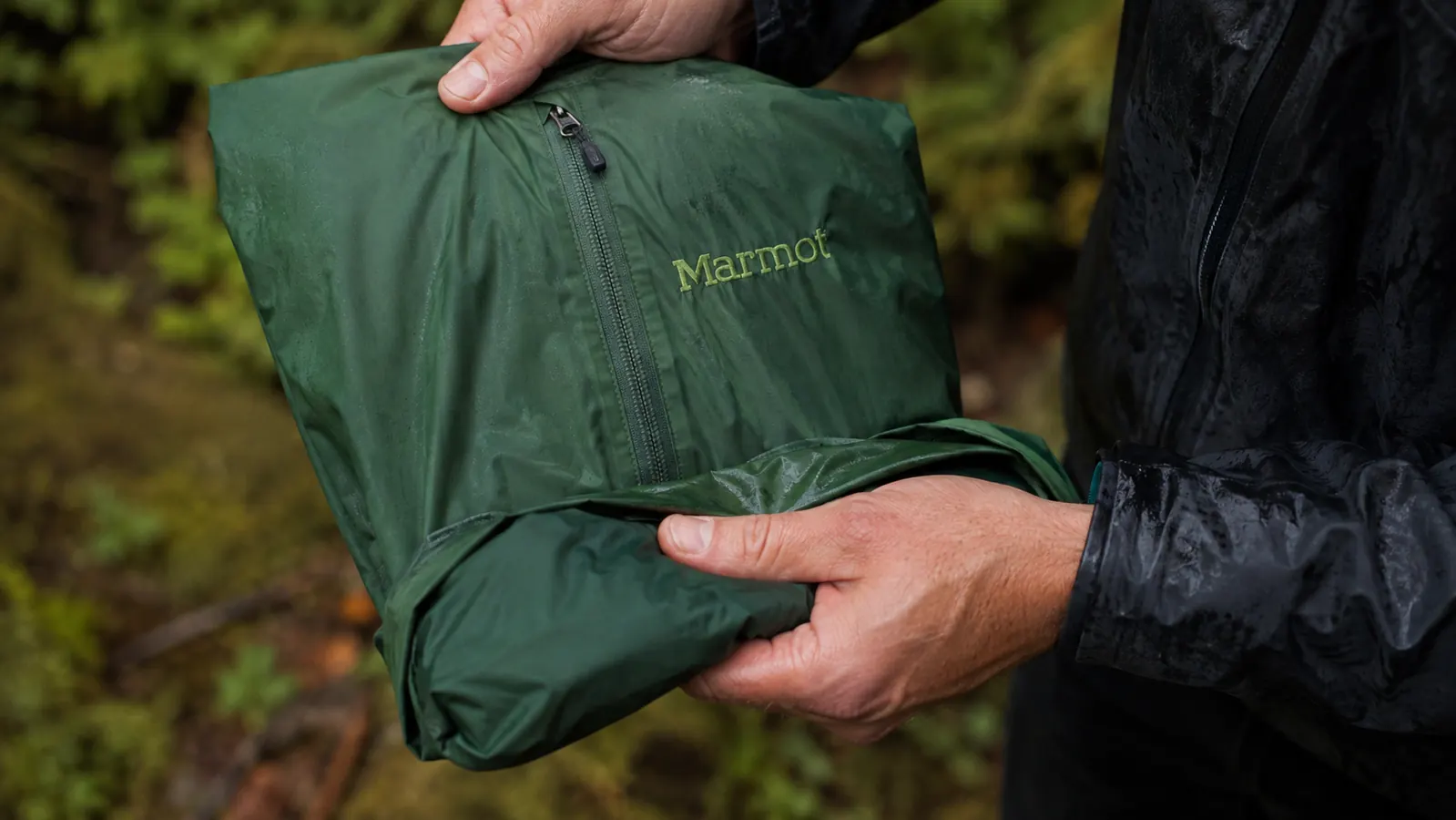 Close-up hand stowing the Marmot Precip Eco into its own left chest pocket